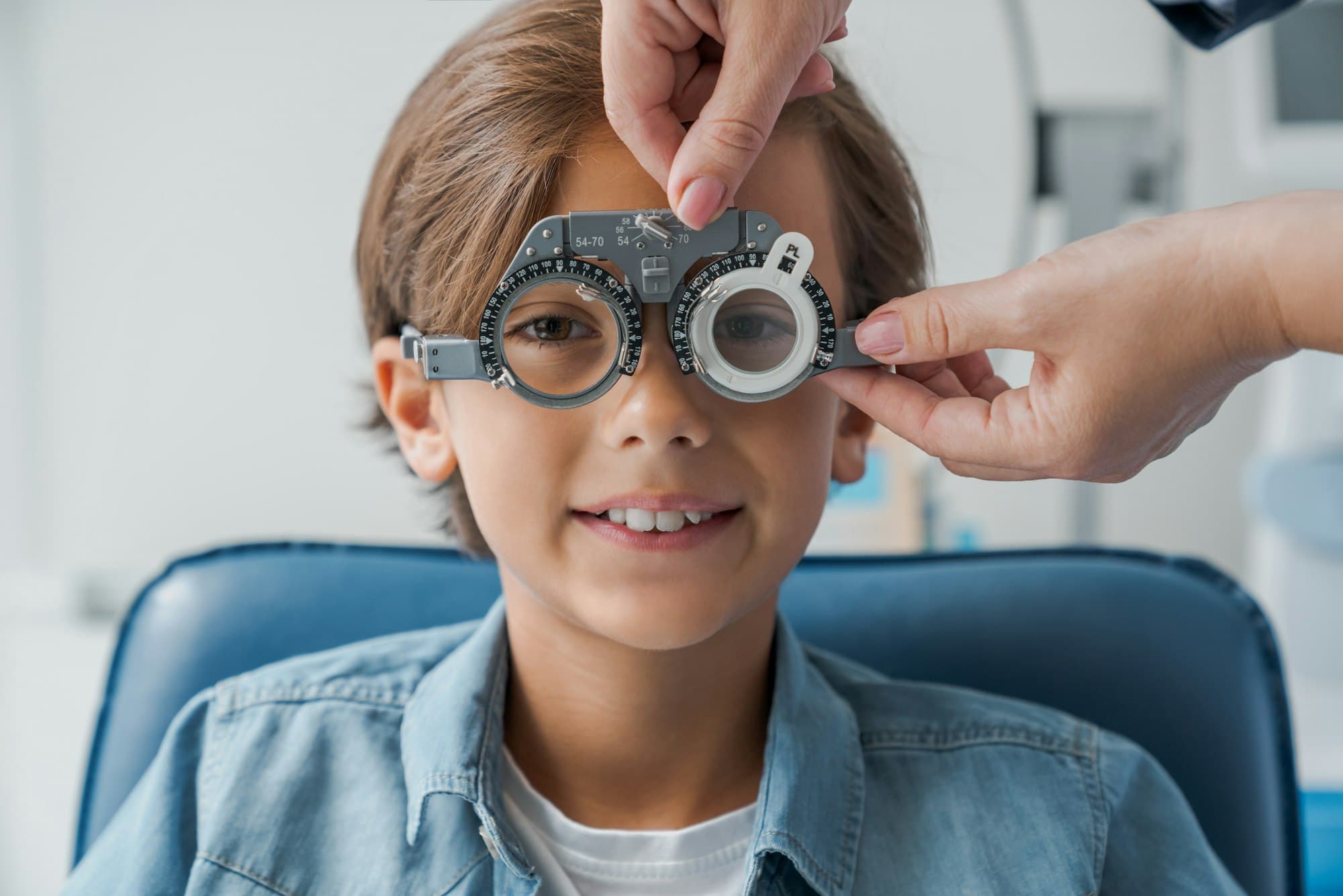 Young boy with phoropter during sight testing eye examinations in ophthalmological clinic.
